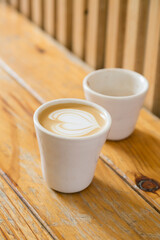 Vertical stills of a cup of flat white coffee on a handmade mug with a latte drawing on top on a wooden table with copy space. Specialty coffee concept.