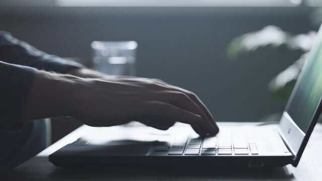 An unrecognizable man uses a laptop to hack into other people's accounts. The hacker is looking for orders on the dark web.