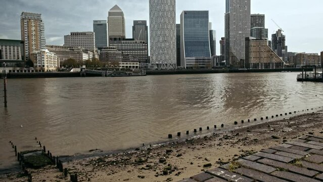 Tilt up from the River Thames to skyscrapers of Canary Wha from Rotherhithe London UK