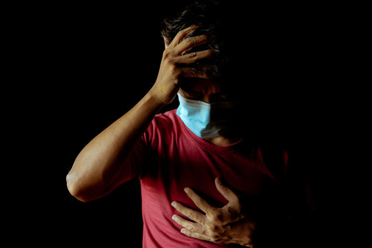Asian man wearing a mask has a headache and has difficulty breathing after contracting Covid-19 even after undergoing treatment.