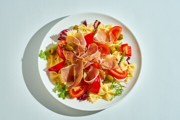 Close-up on pasta with jamon, tomatoes and olives.