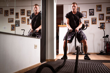 Obraz na płótnie Canvas Man trains at the gym with ropes