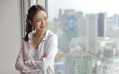 Portrait of confident and beautiful young asian businesswoman with happy smiling face standing and looking away in modern hotel with city blurred background. Success business and lifestyle concept