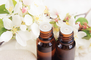 Essential oils glass bottles closeup fresh white apple blossom flowers delicate aromatic petals. Fragrance spa, aromatherapy treatment, herbal skin care cosmetic, light pastel tones.