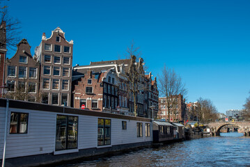 Naklejka premium Amsterdam, Netherlands, April 2022. The canals in Amsterdam with the houseboats and the renovated warehouses.