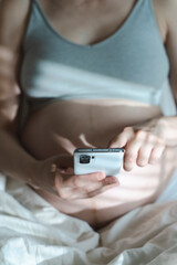 A pregnant woman uses a smartphone while relaxing in her home bed. Internet, shopping, communication during pregnancy and before the birth of a child. Women's and newborn health