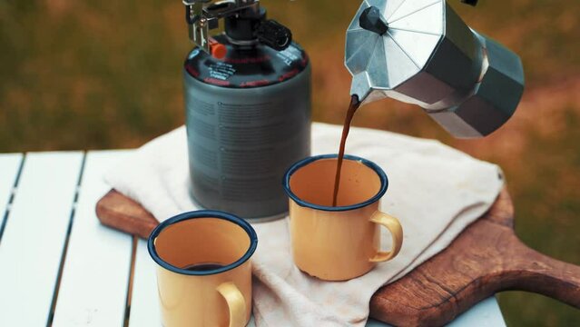 Pouring Coffee from a silver compact metal kettle into a yellow rugged mug while camping