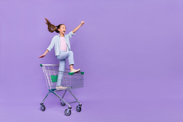 Photo of funny impressed small schoolgirl dressed jeans shirt driving shopping tray empty space...