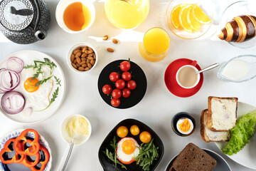 Delicious family breakfast table with coffee, tea, orange juice, croissants, toast, butter, fried and boiled eggs, avocado, cherry tomatoes, almond and salad.