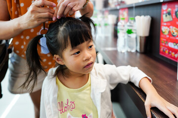 Mother tied daughter's hair. Baby hair tied with colorful rubber bands with two ponytails in front Japanese restaurant before meal time.