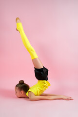 Young gymnast girl stretching and training on a pink background. Sport and healthy lifestyle concept