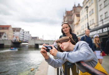 Portrait of happy preteen tourist girl taking photos with camera in town.