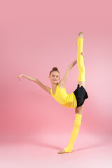 Young gymnast girl stretching and training on a pink background. Sport and healthy lifestyle concept
