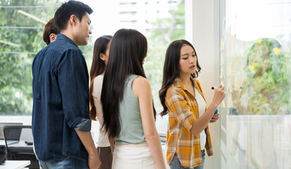 Asian business creative team meeting planning by using post-it notes to share ideas on a glass wall.