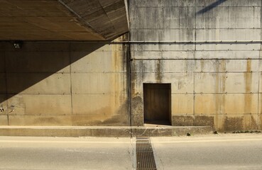 Grunge concrete block wall of a road underpass divided by shadow . Sidewalk and asphalt road in front. Background for copy space