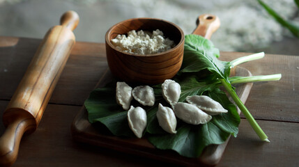 Russian fresh handmade dumplings lying on a wooden table on a cutting board with cottage cheese in...