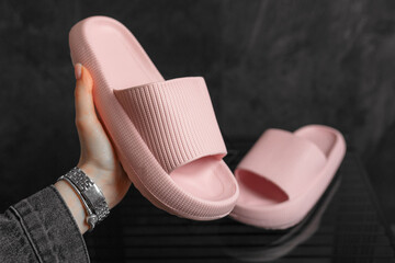 Colorful pink Sandals shoes. Pink flip flops on dark black background. Woman hand hold a shoe