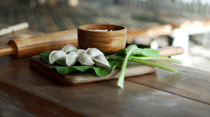 Russian fresh handmade dumplings lying on a wooden table on a cutting board with cottage cheese in a wooden plate and spinach