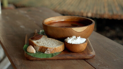 Traditional Russian fresh hot soup borsch with beetroot, red color, with sour cream and fresh bread in a wooden plate standing on a wooden table