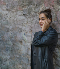 Waist-up shot of a charming Hispanic lady looking away pensively with one hand touching her face while is standing ahead of a stone wall