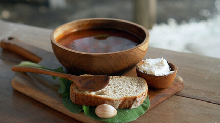 Traditional Russian fresh hot soup borsch with beetroot, red color, with sour cream and fresh bread in a wooden plate standing on a wooden table