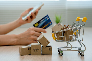 Online shopping-boxes or parcels are placed on the table and shopping carts. Blurred background, woman use credit card to make online purchases on laptop. Online service. New normal shopping delivery.