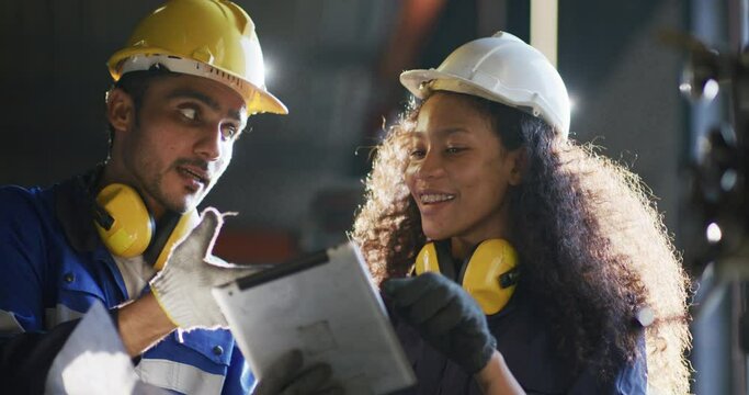 UntitleIndustrial engineer, technician worker wearing uniform, safety hard hat using tablet computer checking control automated robotic arm machine in factory. Automatic manufacturing