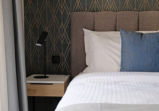 Close-up fragment of bedroom with empty bedside table, reading lamp and a socket in modern interior​ design home or hotel. Soft pillow and blanket, stylish comfortable furniture.