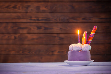 purple birthday cake with burning candles on dark wooden background