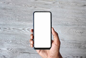 Hand holding smartphone with blank white screen on wooden table background.