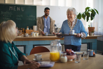 Smiling elderly women enjoying breakfast in nursing home care center.