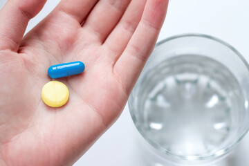 Blue and yellow pill on a hand and glass of a water. Top view. Ukrainian Medical Capsules. Humanitarian medical care. Save Ukraine