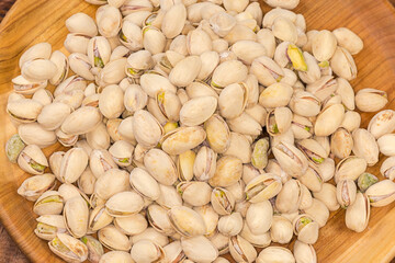 Pile of the roasted salted pistachio nuts on wooden dish