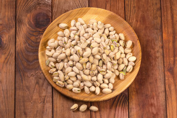 Roasted salted pistachio nuts on wooden dish on rustic table