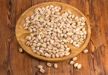 Roasted salted pistachio nuts on wooden dish on rustic table