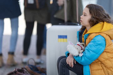 Sad Ukrainian immigrant child with luggage waiting at train station, Ukrainian war concept.