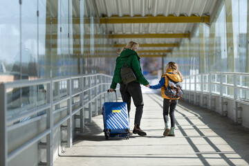 Rear view of Ukrainian immigrant mother with child with luggage walking at train station, Ukrainian...