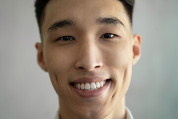 Asian man with dimples smiles widely raising eyebrow in room on blurred background. Portrait of...