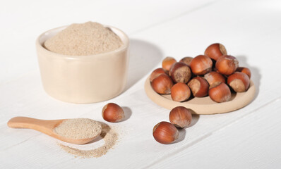 whole raw hazelnuts and hazelnut flour on white wooden table. paleo an ketogenic diet baking, keto...