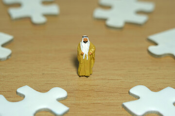 Miniature people toy figure photography. Business alternative concept. A Sultan wearing yellow Bisht (king cloak) standing in the center of four puzzle jigsaw piece. Image photo