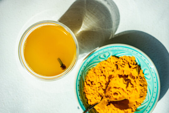 Overhead view of a Shot of turmeric Moon milk with fresh cloves and a bowl of turmeric powder