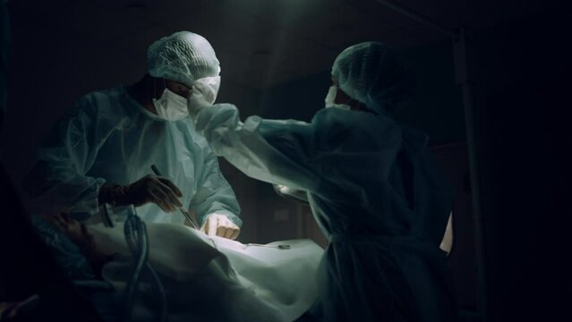 Professional surgeon operating in dark emergency room. Medical team cooperation