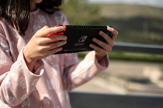 Madrid, Spain - 13 April 2022, girl playing game on Nintendo Switch console in public park