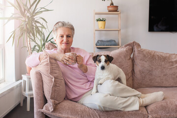 mature older adult grey-haired woman drinking coffee relaxing on sofa at home