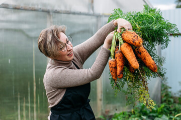 young woman farmer harvesting carrots from the soil © Стэвия Горошкина