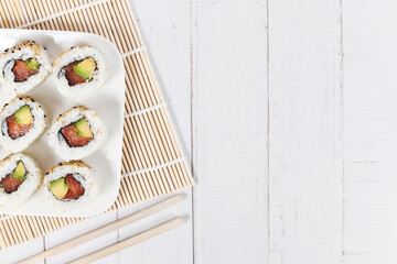 Sushi inside out rolls with salmon, avocado and sesame on side of wooden table