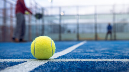 Yellow ball on floor behind paddle net in blue court outdoors. Padel tennis