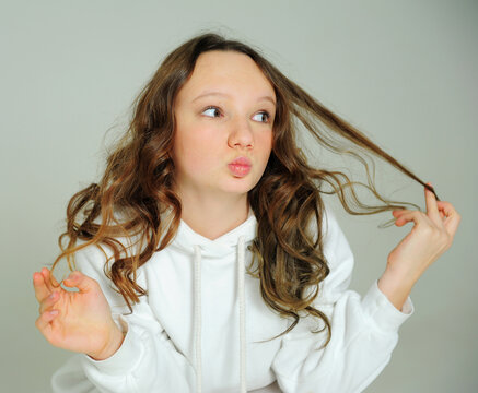 teenage girl in a white hoodie in the studio on a white background stands faces and various grimaces, she is beautiful and young. High quality photo