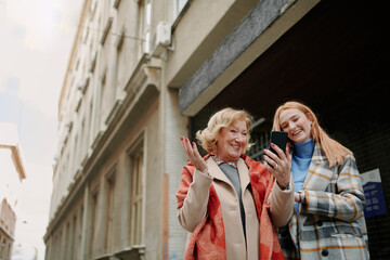A grandmother and her grandchild standing on the street and reading messages on the phone.