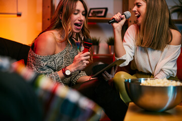 Two beautiful young women are singing karaoke at a home party.